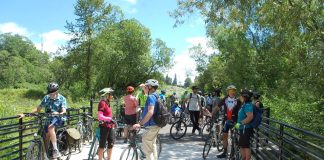 Join The Urbanist for Campaign Events Ahead of the November Election A group of over dozen people with their bikes on a wetland boardwalk segment of the trail.