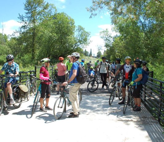 Join The Urbanist for Campaign Events Ahead of the November Election A group of over dozen people with their bikes on a wetland boardwalk segment of the trail.