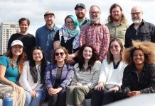 Apply to Join The Urbanist Election Committee The group stands on a rooftop with the Seattle skyline and Elliott Bay in the background.