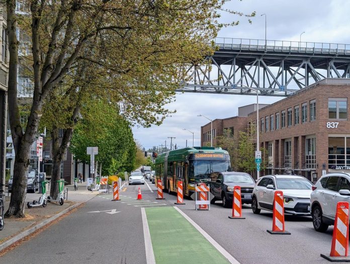 Route 62 bus in 34th Street Traffic Fremont - Trumm 20250513 The view east up N 34th Street with the steel-spanned Aurora Avenue bridge in the distance.