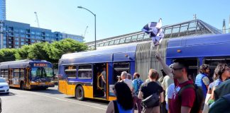 A group of pedestrians that raced the Route 8 with two buses in the background.