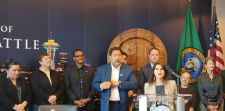 Rinck stands at the lectern and a group of supporters stands behind her, including colleagues Rob Saka and Sara Nelson and Mayor Bruce Harrell.