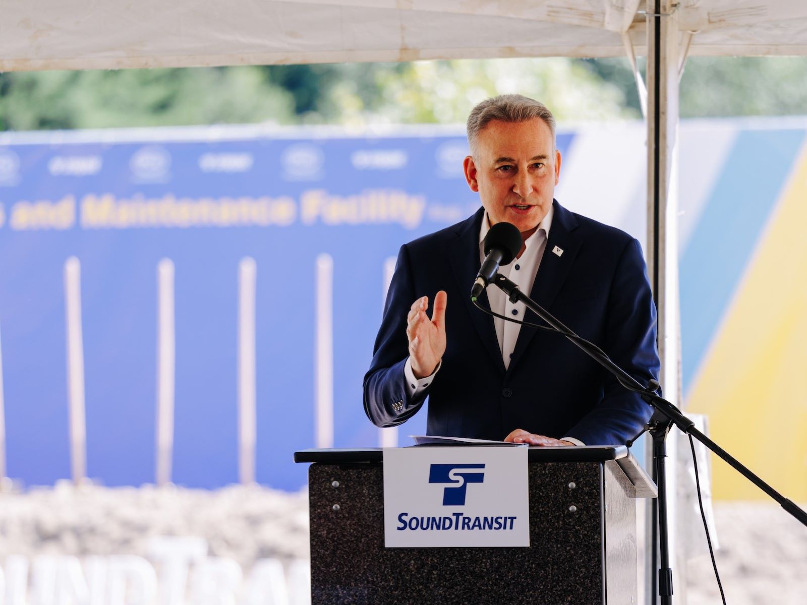 Dow stands at the lectern with a row of shovels and a ceremonial mound of dirt in the background. 