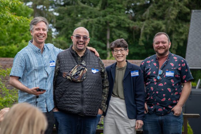 The four candidate stand in a line smiling with trees in the background.