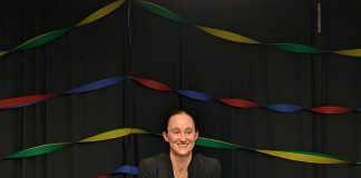 Wilson stands in front of a lectern with her yellow campaign sign with rainbow streamers behind her.