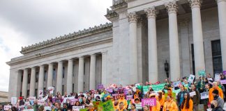 Op-Ed: Tech Workers Must Challenge the Political Power of Their Bosses More than 100 advocates hold signs urging a balanced tax code on the steps of the state Capitol building with its many marble columns.