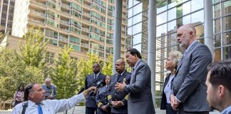 Officials including Bob Kettle and Debora Juarez and SPD top brass stand on the steps of Seattle's US Courthouse with a reporter outstretching an arm holding a mic to interview them