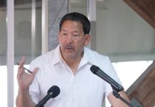 Harrell Pledges Seattle Will Be AI Leader, Plan Fuzzy on Details Wearing a white polo Harrell stands at a lectern gesturing with a pen in his hand.