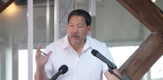 In Last Stand, Harrell Intensifies Negative Attacks on Wilson Wearing a white polo Harrell stands at a lectern gesturing with a pen in his hand.