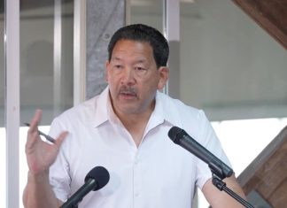 In Last Stand, Harrell Intensifies Negative Attacks on Wilson Wearing a white polo Harrell stands at a lectern gesturing with a pen in his hand.