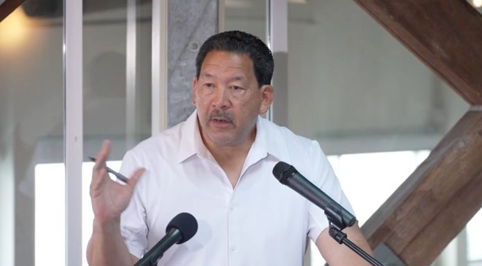 In Last Stand, Harrell Intensifies Negative Attacks on Wilson Wearing a white polo Harrell stands at a lectern gesturing with a pen in his hand.