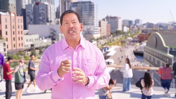 Harrell weather a pink button up shirt with pedestrians on the Overlook Walk in the background.