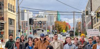 More than two dozen advocates stand behind Rinck at the bus stop at 12th Avenue and Union Street, with Madison Street in the background.