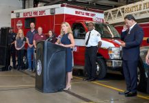 Sales Tax Hike Would Fund Civilian Responder Expansion, Barring SPOG Obstruction Barden stands at a lectern at a fire hall with a fire truck, fire chief, mayor, and CARE staff in the background.