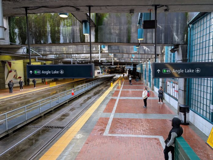 International District Station passengers on platform - The Urbanist 20250305 A view of the platform at International District Station from partway up the escalator. A few dozens passengers are waiting for trains.