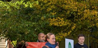 Wilson holds a mic and two volunteers who banners for The Urbanist and for Seattle Tech4Housing.