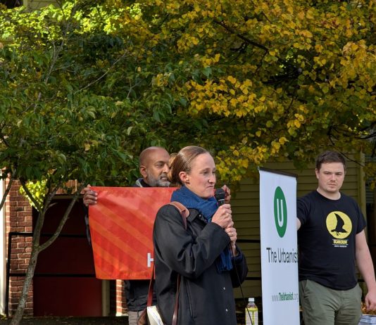 Wilson Maintains Lead over Harrell, Two New Polls Indicate Wilson holds a mic and two volunteers who banners for The Urbanist and for Seattle Tech4Housing.