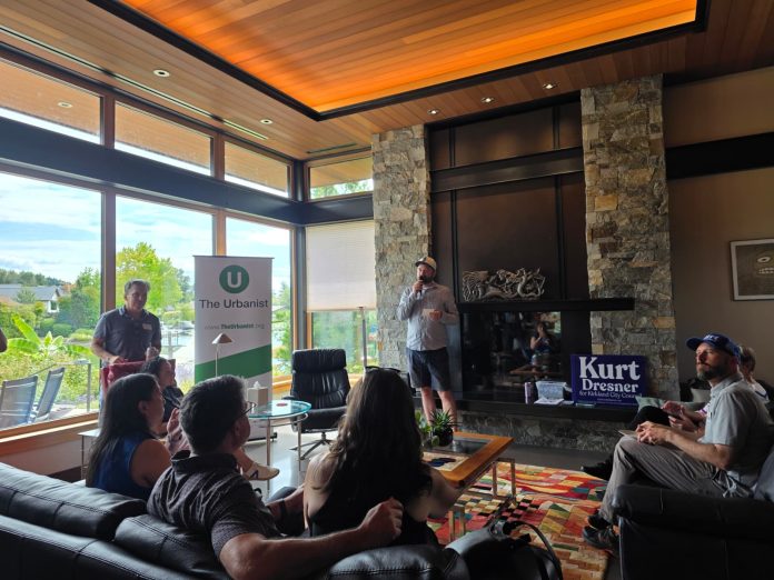 Urbanst August Endorsed Candidae Party Doug Trumm speaks in front of a group of urbanist supporters with a fireplace behind.