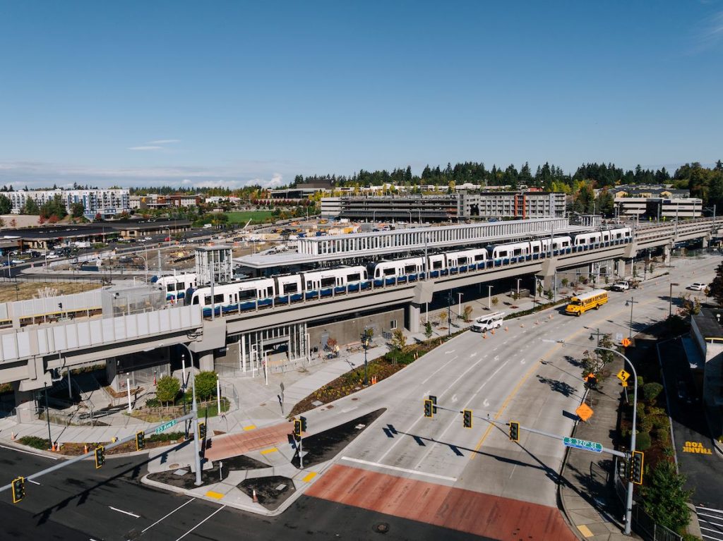 A drone photo shows a four-car train at Federal Way Station during testing. Some mid-rise buildings are off in the distance.