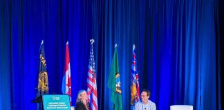 Op-Ed: Ferguson Must Back ‘Stand Up to Trump’ Rhetoric with Funding Ferguson and Smith sit on white lounge chairs with a row of flags behind them for the Cascadia states and nations.