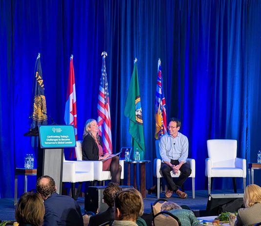 Op-Ed: Ferguson Must Back ‘Stand Up to Trump’ Rhetoric with Funding Ferguson and Smith sit on white lounge chairs with a row of flags behind them for the Cascadia states and nations.