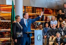 Harrell Concedes to Wilson, Ushering in a New Era in Seattle Harrell waves goodbye at the end of his speech with his wife on his arm. They stand at a lectern in the lobby of city hall.