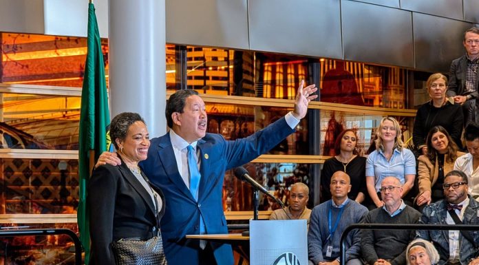 Harrell Concedes to Wilson, Ushering in a New Era in Seattle Harrell waves goodbye at the end of his speech with his wife on his arm. They stand at a lectern in the lobby of city hall.