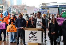 ‘Build the Damn Trains’ Campaign Pushes Sound Transit Toward Creative Solutions Advocates wave "build the damn trains sign" and Kirk from Transportation Choices Coalition speaks at the lectern