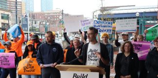 Advocates wave "build the damn trains sign" and Kirk from Transportation Choices Coalition speaks at the lectern