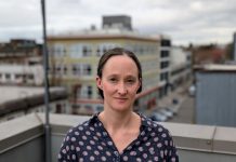 Katie Wilson Takes 91-Vote Lead in Dramatic Seattle Mayor Race Wilson stands on a rooftop in Capitol Hill wearing a Mona Lisa smile. She's a White middle-aged woman with dark hair.
