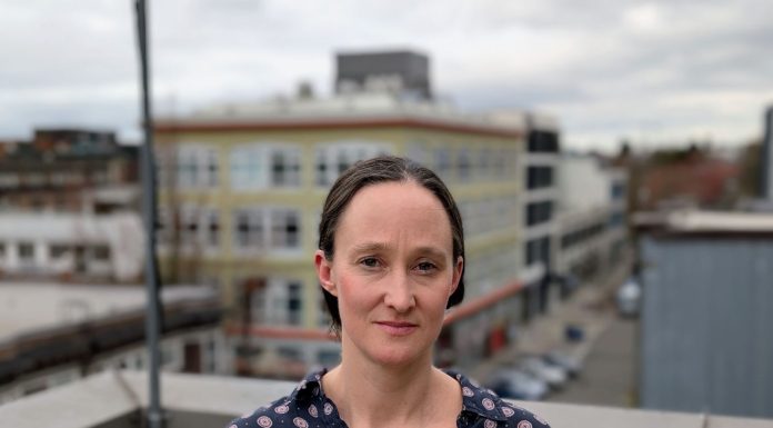 Katie Wilson Charts New Course on Public Safety and Homelessness Wilson stands on a rooftop in Capitol Hill wearing a Mona Lisa smile. She's a White middle-aged woman with dark hair.