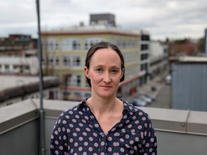 Katie Wilson Capitol Hill portrait _Doug Trummn 20250310 Wilson stands on a rooftop in Capitol Hill wearing a Mona Lisa smile. She's a White middle-aged woman with dark hair.