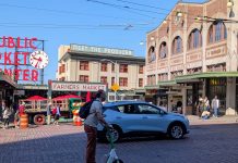 Seattle Scootershare Ridership Continues to Surge, as Critics Make Regulatory Push A person rides a Lime scooter on First Avenue in front of Pike Place Market with an SUV passing in the other lane.