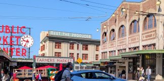 Seattle Scootershare Ridership Continues to Surge, as Critics Make Regulatory Push A person rides a Lime scooter on First Avenue in front of Pike Place Market with an SUV passing in the other lane.