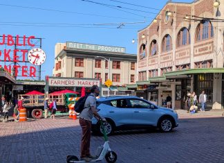 Seattle Scootershare Ridership Continues to Surge, as Critics Make Regulatory Push A person rides a Lime scooter on First Avenue in front of Pike Place Market with an SUV passing in the other lane.