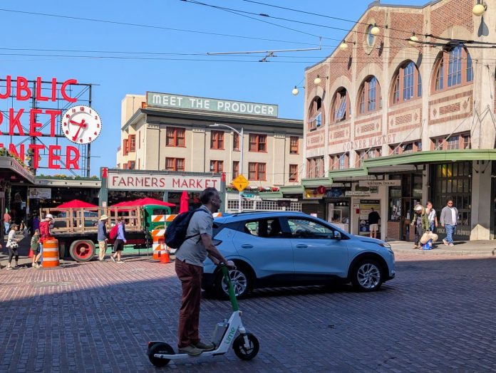 Scooter rider by Pike Market - Trumm 20250717 A person rides a Lime scooter on First Avenue in front of Pike Place Market with an SUV passing in the other lane.