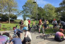 Join Us for The Urbanist’s November and December Events About a dozen people are pictured sitting or standing with their bikes in a park.