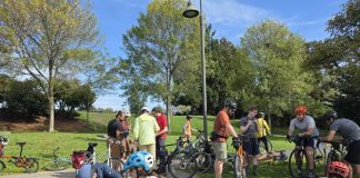 Join Us for The Urbanist’s November and December Events About a dozen people are pictured sitting or standing with their bikes in a park.