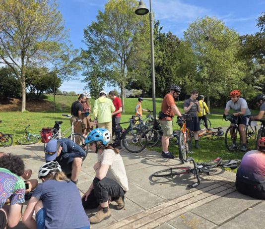 Join Us for The Urbanist’s November and December Events About a dozen people are pictured sitting or standing with their bikes in a park.