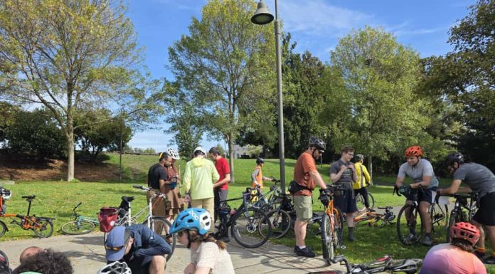 Join Us for The Urbanist’s November and December Events About a dozen people are pictured sitting or standing with their bikes in a park.