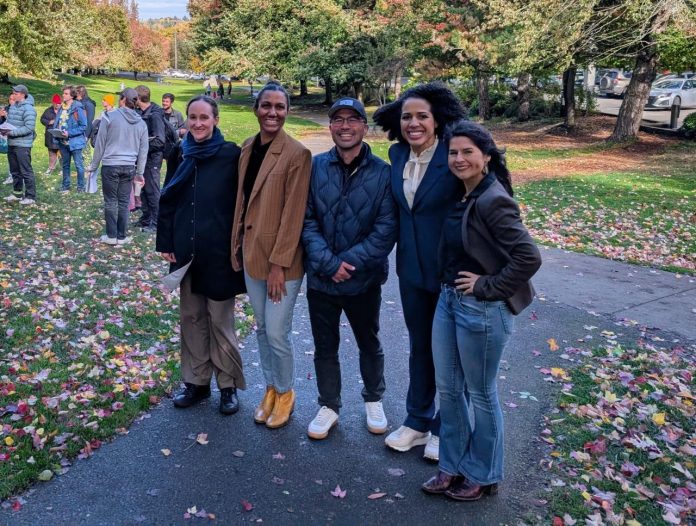 The five candidates stand shoulder to shoulder in Columbia Park, which is lined with trees in full autumn colors.