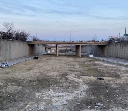 Book Review: How a Highway Map Wrecked Baltimore A barren trenched has an access road on the city but empty field down the middle with bridges spanning the trench to connect the street grid.