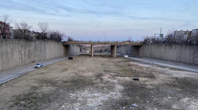 Book Review: How a Highway Map Wrecked Baltimore A barren trenched has an access road on the city but empty field down the middle with bridges spanning the trench to connect the street grid.