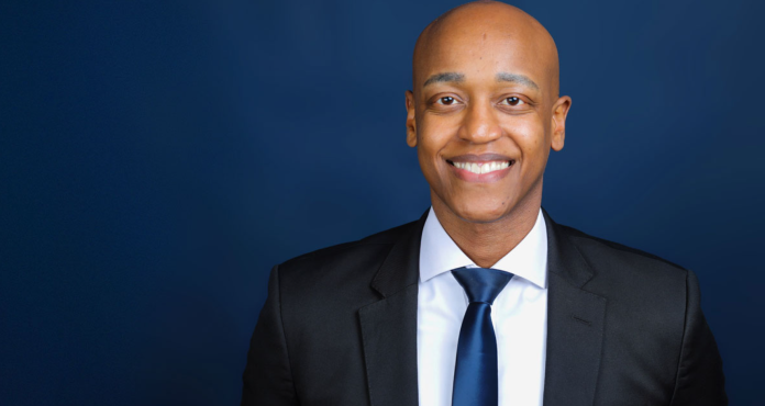 Girmay Zahilay, a Black millennial man wearing a suit, standing in front of a blue background
