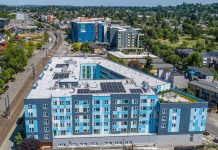 Affordable Housing Expands in Seattle’s Central District and South End An aerial view of a six-story light blue building with a central court and the light rail line just to the west.