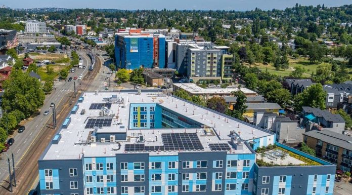 Affordable Housing Expands in Seattle’s Central District and South End An aerial view of a six-story light blue building with a central court and the light rail line just to the west.