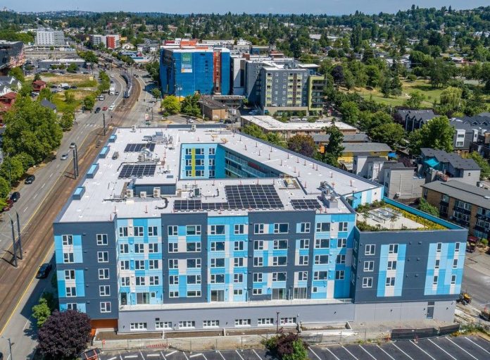 nichols court aerial by LIHI An aerial view of a six-story light blue building with a central court and the light rail line just to the west.