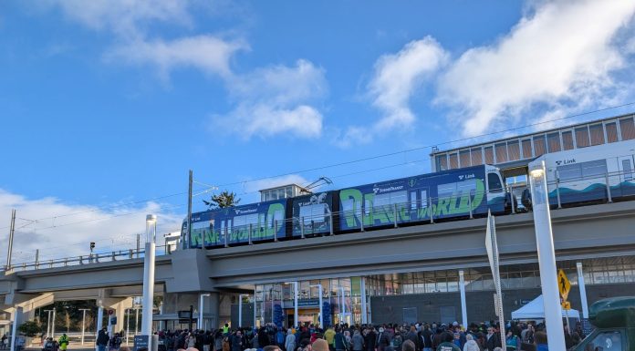 Urbanist Podcast: A Light Rail Opening and Police Accountability Door Closing A line of people approach Federal Way Downtown Station, with a train waiting at the elevated platform.