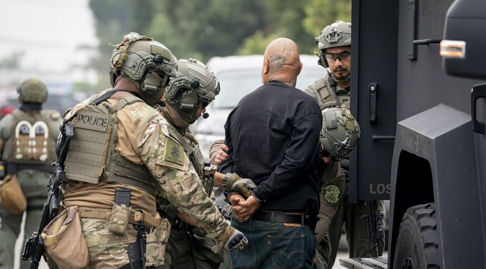 UW Report: Immigration Agents Still Accessing WA Driver Data An image of I.C.E. "enforcement and removal operation" in Los Angeles provided by the Department of Homeland Security shows three large agents in camo and battle helmets handcuffing a bald man.