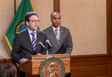 Washington State Reacts to Feared ICE Invasion, Constitutional Crisis Ferguson stands at the lectern with Brown over his shoulder. Both wear suits and ties.